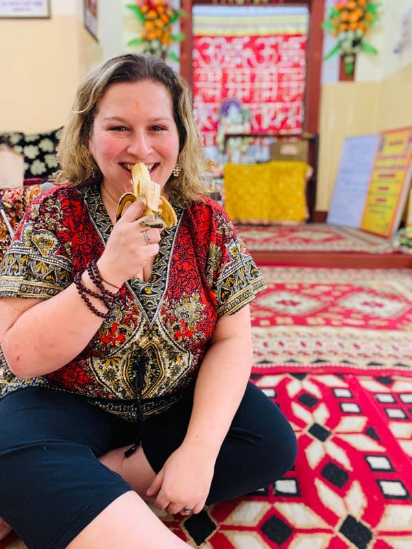 Dr. Jamie Marich eating a banana in a colorful room.