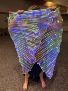 Dr. Jamie wrapped in a lit, rainbow sparking cloth similitude to a cocoon