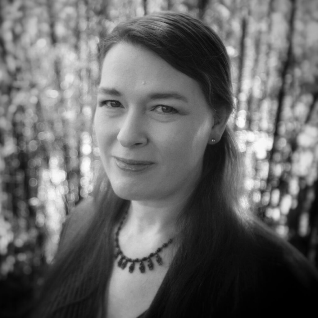 Judi's headshot A black and white photo of a woman standing in front of bamboo.