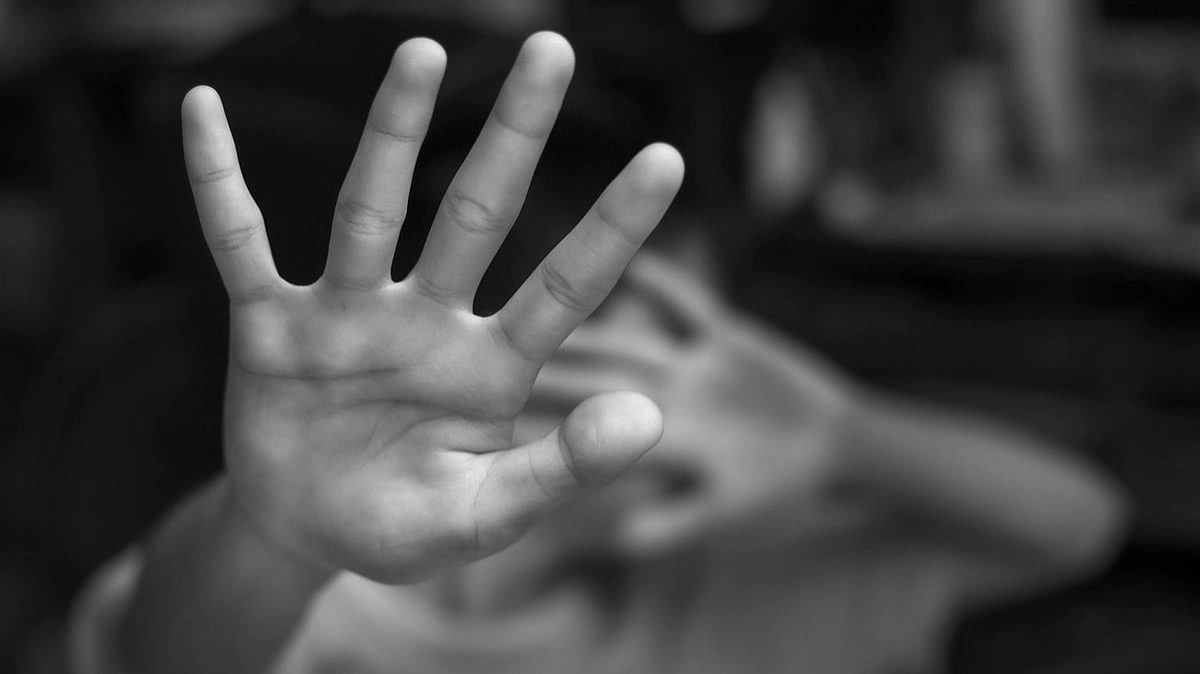 Black-and-white photo of a person holding one hand up toward the camera, palm open and fingers spread, partially obscuring their face in the background.