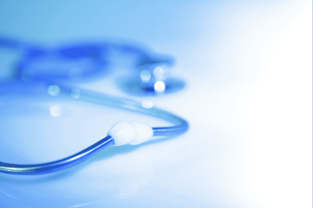 A close-up, softly blurred image of a blue stethoscope resting on a light surface, with focus on the tubing and earpiece while the chest piece fades into the background.