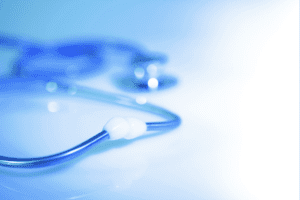 A close-up, softly blurred image of a blue stethoscope resting on a light surface, with focus on the tubing and earpiece while the chest piece fades into the background.