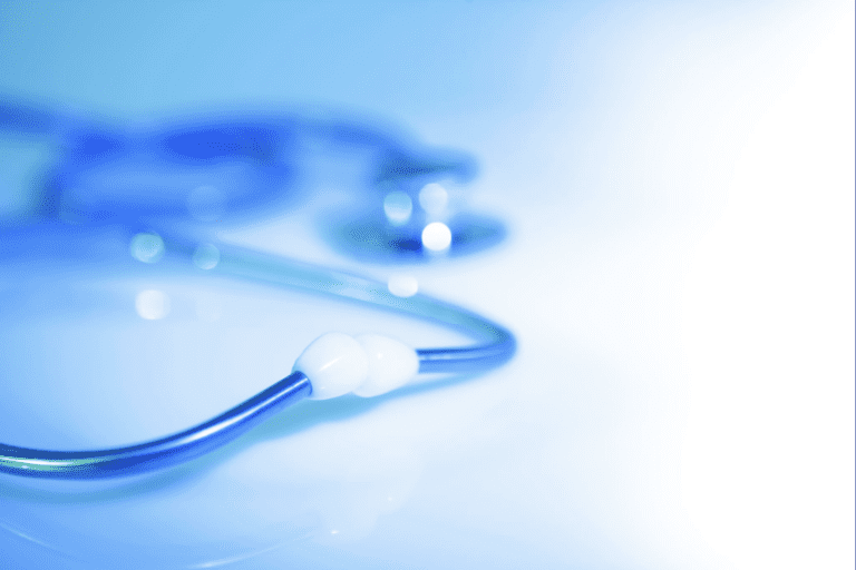 A close-up, softly blurred image of a blue stethoscope resting on a light surface, with focus on the tubing and earpiece while the chest piece fades into the background.