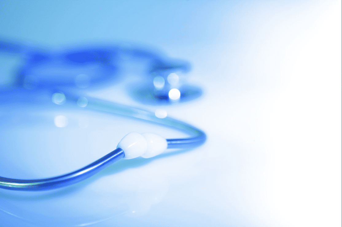 A close-up, softly blurred image of a blue stethoscope resting on a light surface, with focus on the tubing and earpiece while the chest piece fades into the background.